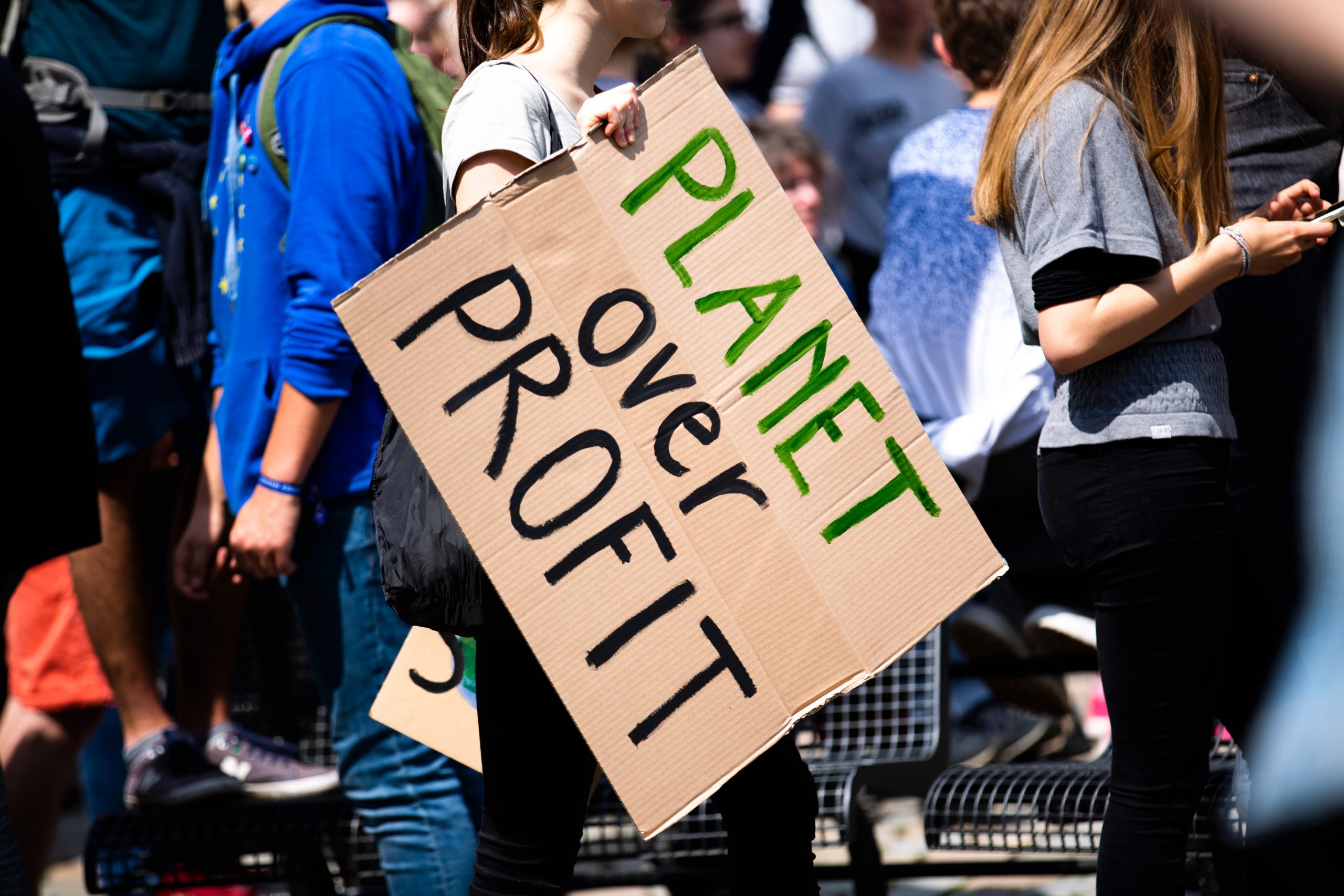 Image of a climate protester holding a sign reading 'Planet over Profit'.