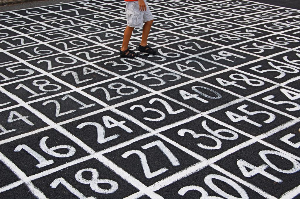 Numbers written across concrete in chalk with the view of a child's feet walking across the numbers