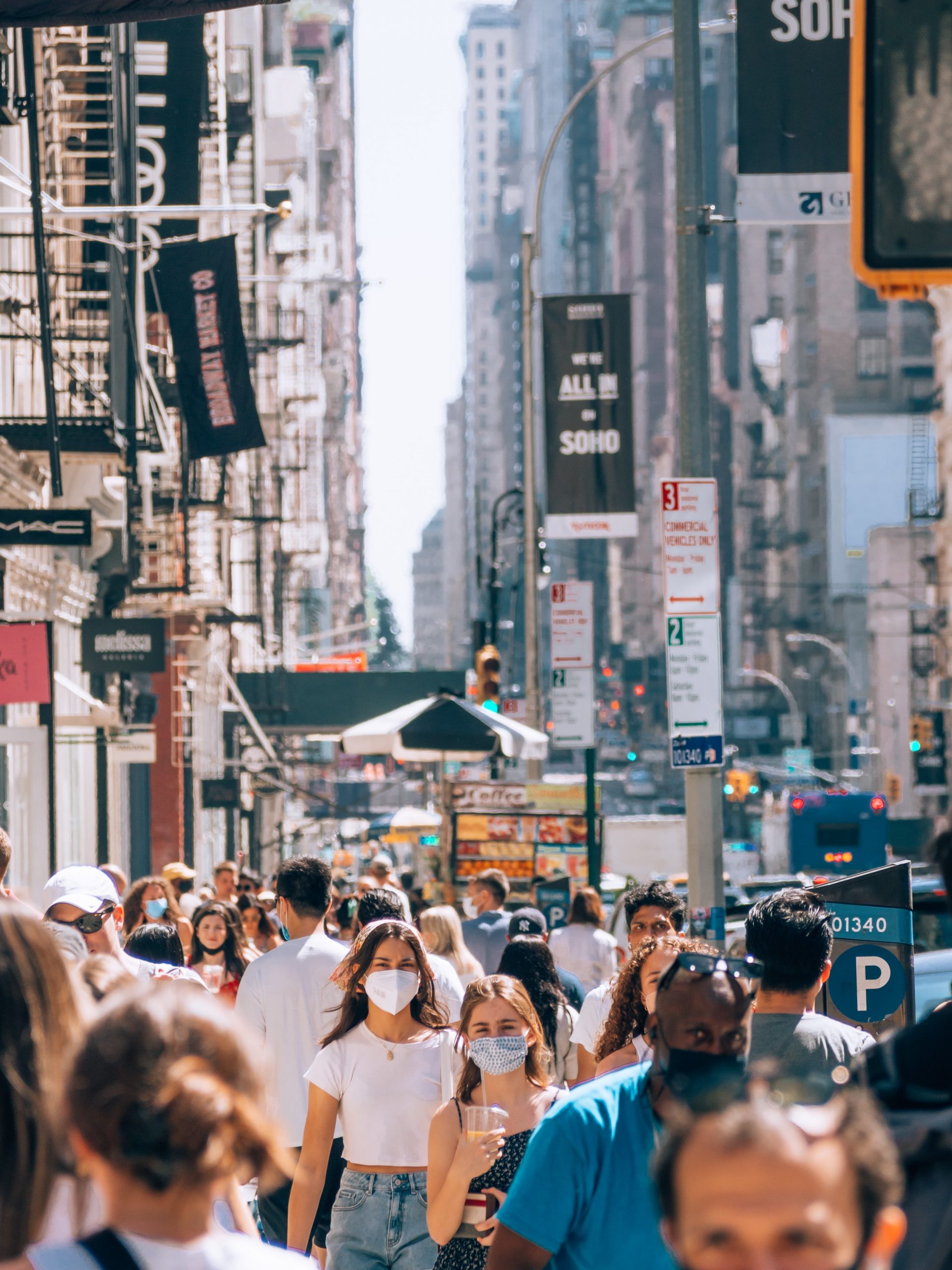 Image of a busy street, possibly in New York City, with lots of people walking down the street while wearing face masks.